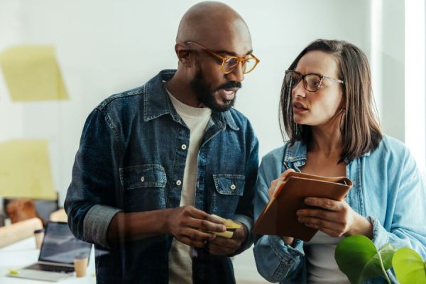 Dekoratives Bild: Zwei Personen diskutieren in einer Bürosituation.