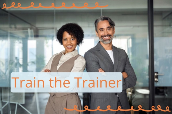 Zwei Personen stehen in einem Büro, Rücken an Rücken gelehnt, die Arme verschränkt. Im Vordergrund befindet sich das Thema des Beitrages als Schriftzug: Train the Trainer