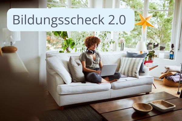 Eine Person sitzt arbeitend am Laptop auf einem Sofa. Im Hintergrund befindet sich eine Fensterfront nach draußen. 